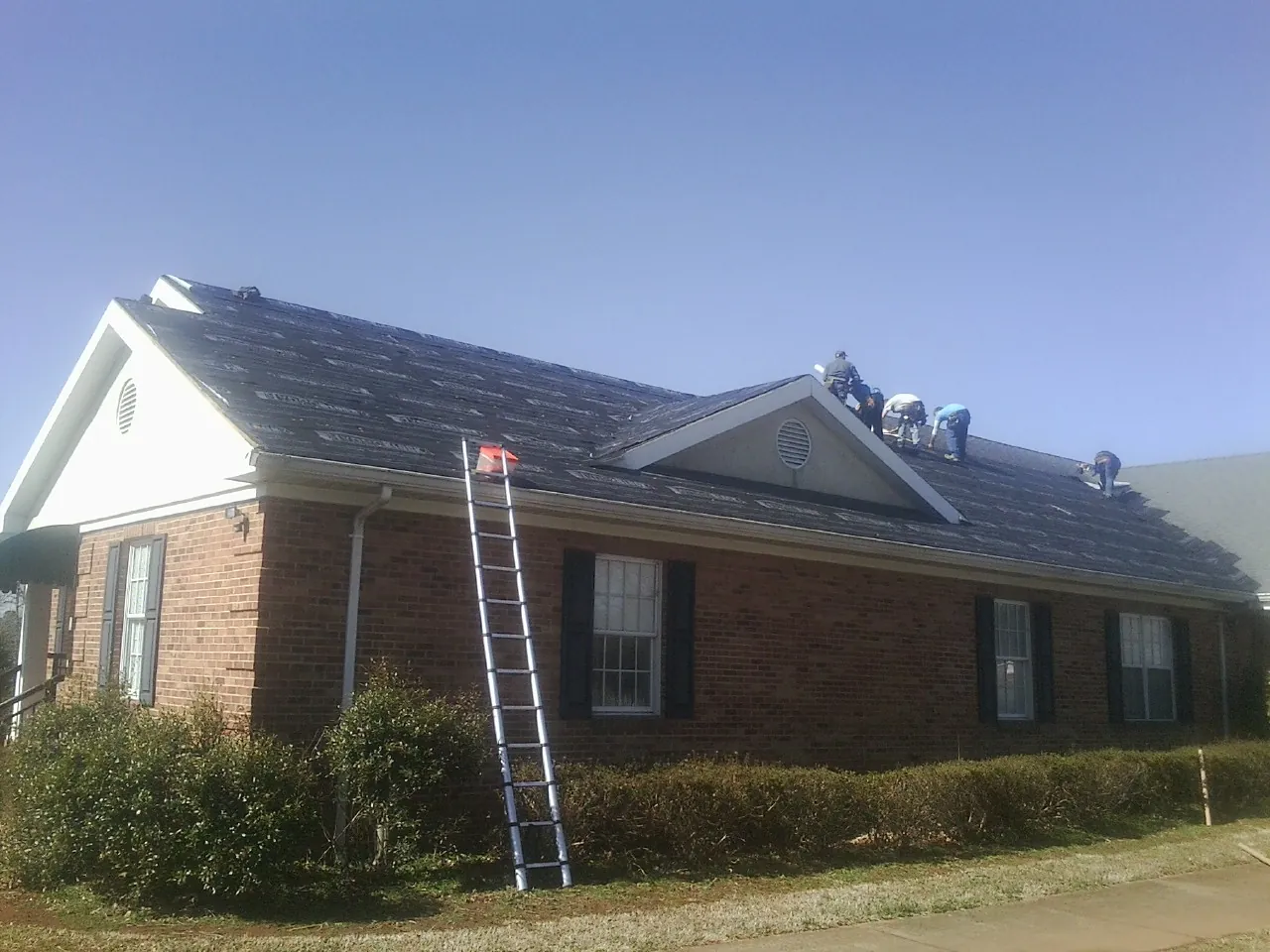 Crew tearing shingles off a brick ranch roof with a ladder set — Emergency Roof Repair work by our crew in Chalfont