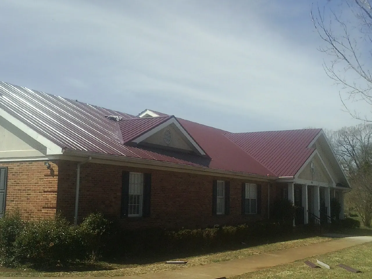 Red metal roof with gabled entries on a long brick building, from a Hail Damage Roof Repair job in Chalfont