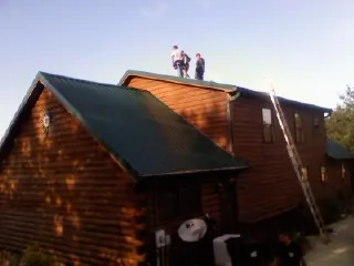 Crew on the ridge of a green metal roof on a two story log home in Chalfont