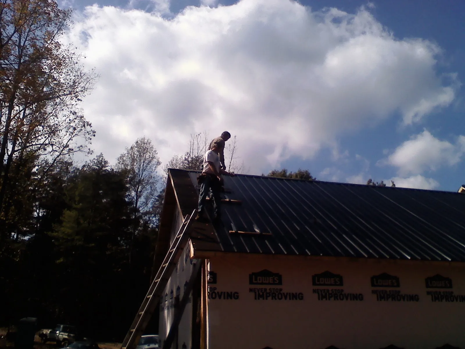 Roofer fastening dark metal panels high against a cloudy sky, from a Roof Inspection job in Chalfont
