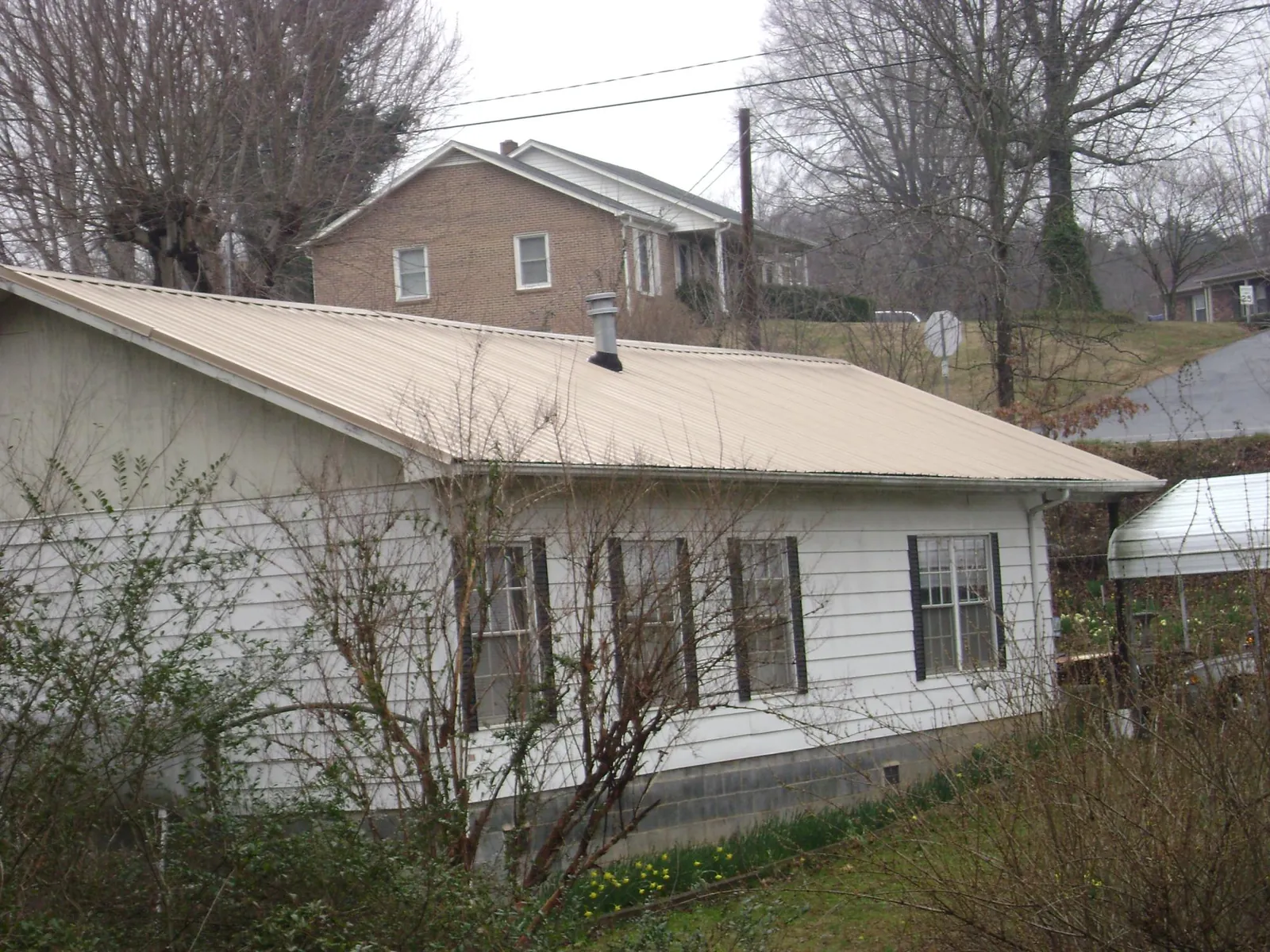 Tan metal roof on a white sided house set into a hillside — Commercial Roofing by Roofing Brothers in Chalfont